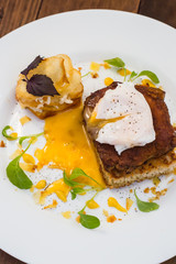 Dish with meat steak on toast, potato chips  melted cheese and poached egg  Dutch sauce. Wooden background. Top view. Close-up