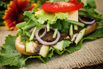Sandwich with veal steak, greens, zucchini, tomatoes, cheese and mustard sauce. Wooden background. Close-up. Selective focus