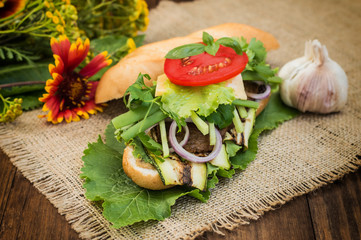 Sandwich with veal steak, greens, zucchini, tomatoes, cheese and mustard sauce. Wooden background. Close-up. Selective focus