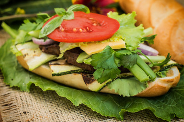 Sandwich with veal steak, greens, zucchini, tomatoes, cheese and mustard sauce. Wooden background. Close-up. Selective focus