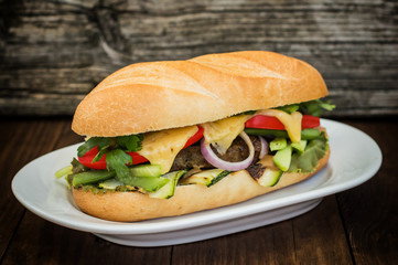 Sandwich with veal steak, greens, zucchini, tomatoes, cheese and mustard sauce. Wooden background. Close-up. Selective focus