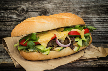 Sandwich with veal steak, greens, zucchini, tomatoes, cheese and mustard sauce. Wooden background. Close-up. Selective focus