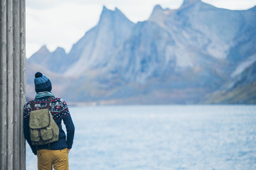 A man with a backpack standing on a wooden pier. Pier in the sea of the Gulf, around the Bay of high rocky mountains. Traveler, traveling, nature. Copy space.