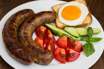 Nutritious breakfast consisting of fried sausage,  eggs, toast, fresh cucumbers and tomatoes. Wooden rustic background. Top view. Close-up