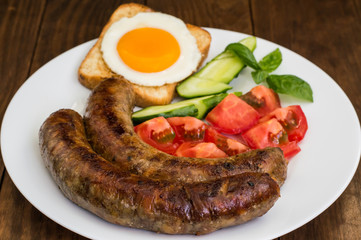 Nutritious breakfast consisting of fried sausage,  eggs, toast, fresh cucumbers and tomatoes. Wooden rustic background. Top view. Close-up