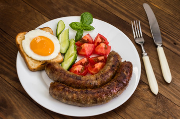 Nutritious breakfast consisting of fried sausage,  eggs, toast, fresh cucumbers and tomatoes. Wooden rustic background. Top view. Close-up