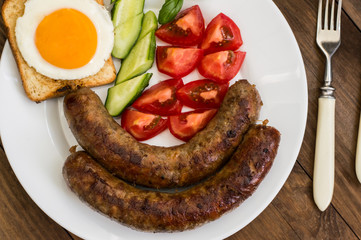 Nutritious breakfast consisting of fried sausage,  eggs, toast, fresh cucumbers and tomatoes. Wooden rustic background. Top view. Close-up