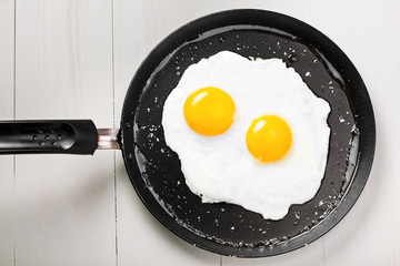 Two fried eggs in a frying pan cooked for breakfast. Delicious international meal on a table. Homemade food, top view.