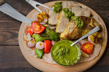 Meat with vegetables, grilled and served  Italian Salsa Verde sauce. Wooden rustic table. Close-up