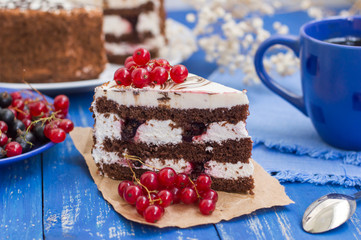 Biscuit cream cake with cherries and red currants. Wooden background. Close-up