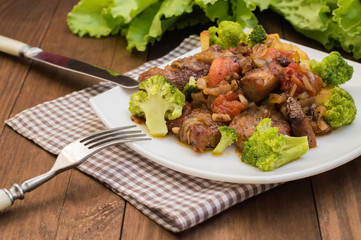 Stifado - a traditional Cypriot dishes, spread in Greece. It consists of  stew with tomatoes, potatoes, broccoli, onions, garlic and spicy spices. Wooden rustic table. Top view. Close-up