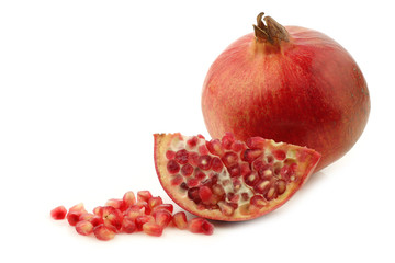 one whole pomegranate(Punica granatum), a cut piece and seeds on a white background