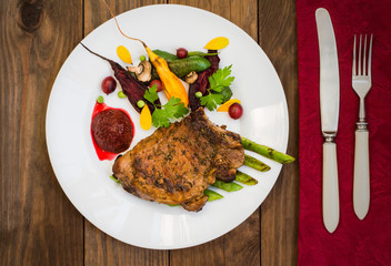 Fried Grilled pork steak on the bone with vegetables, mashed beetroot and berry sauce. Wooden background. Top view. Close-up