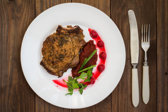 Fried Grilled pork steak on the bone with vegetables, mashed beetroot and berry sauce. Wooden background. Top view. Close-up