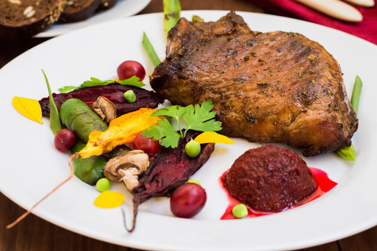Fried Grilled pork steak on the bone with vegetables, mashed beetroot and berry sauce. Wooden background. Top view. Close-up