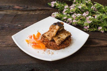 Fish coated in crumbs on vegetable cushion with squash, tomatoes, carrots and onions. Wooden rustic background. Close-up