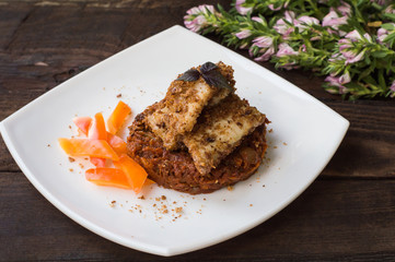 Fish coated in crumbs on vegetable cushion with squash, tomatoes, carrots and onions. Wooden rustic background. Close-up