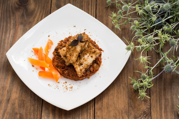 Fish coated in crumbs on vegetable cushion with squash, tomatoes, carrots and onions. Wooden rustic background. Close-up