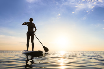 Girl stand up paddle boarding (sup) on quiet sea, sunset - obrazy, fototapety, plakaty