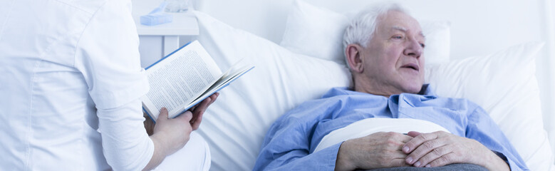 Nurse reading to elderly patient - obrazy, fototapety, plakaty