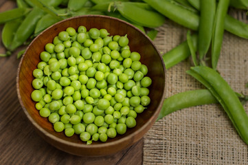 Pea pods in a wooden bowl on sacking.  background. Top view. Close-up