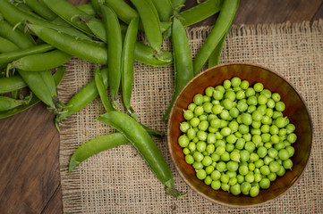 Pea pods in a wooden bowl on sacking.  background. Top view. Close-up