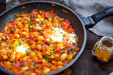 Shakshuka in a Pan, Fried Eggs with Tomato, Paprika, Beans and Parsley on Wooden Table, Top View
