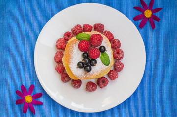 Pancakes with raspberries, currants, sugar and mint. Blue background. Top view. Close-up