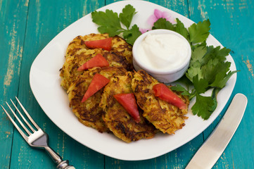 Zucchini Pancakes with sour cream, tomatoes and herbs. Wooden background. Close-up