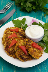 Zucchini Pancakes with sour cream, tomatoes and herbs. Wooden background. Close-up