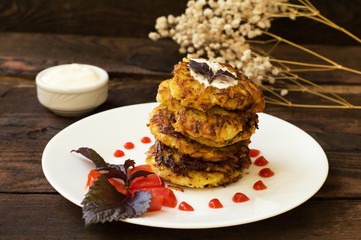 Zucchini Pancakes with sour cream, tomatoes and herbs. Wooden background. Close-up