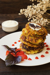 Zucchini Pancakes with sour cream, tomatoes and herbs. Wooden background. Close-up