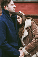 Young happy couple laughing and enjoying christmas street decorations with cookies, cacao, handmade wooden table and red brick wall