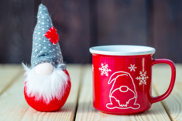 Christmas Greeting Card with Noel Christmas Gnome and Red Cup of Hot Tea or Chocolate or Coffee Drink on the Wooden Background