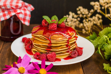 Pancakes with raspberry jam and fresh berries. Wooden background. Close-up