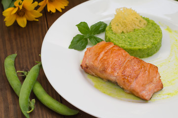 Grilled salmon steak with pea puree, cheese crisps and basil on a plate  the sauce. Wooden rustic background. Top view. Close-up