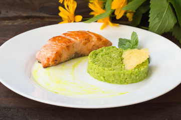 Grilled salmon steak with pea puree, cheese crisps and basil on a plate the sauce. Wooden rustic background. Close-up
