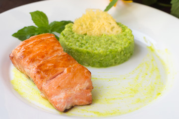 Grilled salmon steak with pea puree, cheese crisps and basil on a plate the sauce. Wooden rustic background. Close-up