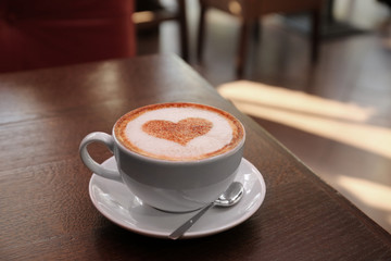 Cup with hot tasty coffee on wooden table in cafe, close up view