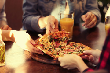 Friends taking slices of tasty pizza from plate, close up view