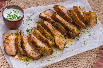 Pork steak cooked on the grill, marinated in herbs and rosemary, served  a table with tzatziki sauce. Background paper for baking. Top view. Close-up