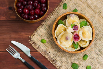 Dumplings with a cherry and mint leaves on  background of flowers  burlap. Wooden table. Top view. Close-up