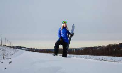 Young woman and her snowboard on snow-covered mountainside at sunset