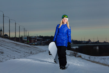 Young woman and her snowboard on snow-covered mountainside at sunset