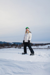 Fototapeta na wymiar Young woman and her snowboard on snow-covered mountainside at sunset
