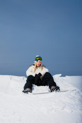 Young woman sitting on snow-covered mountainside with her snowboard 