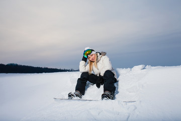 Fototapeta na wymiar Young woman sitting on snow-covered mountainside with her snowboard 