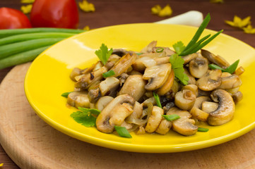 Fried mushrooms on a yellow plate. Wooden background. Close-up