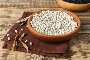 Bowl with white haricot beans and napkin on wooden table