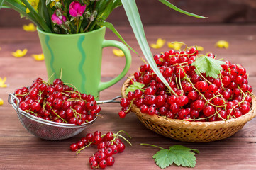 Red currants on a background of flowers. Wooden table. Close-up